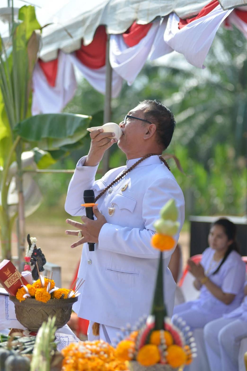 ชายสวมชุดขาวเป่าสังข์ในพิธีการ